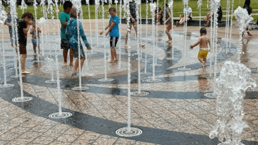 A young child plays in a splash pad at Liz Carpenter Fountain in Austin as families seek relief from extreme heat.