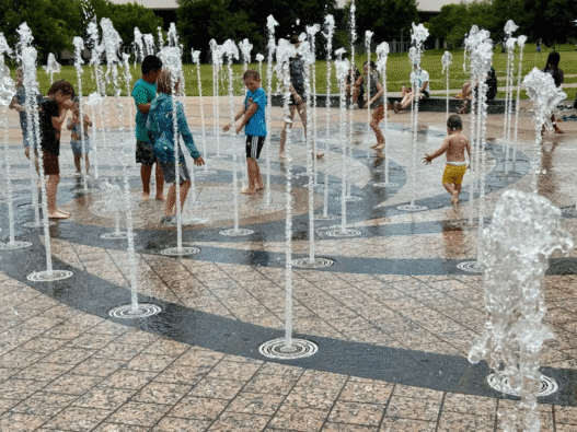 A young child plays in a splash pad at Liz Carpenter Fountain in Austin as families seek relief from extreme heat.