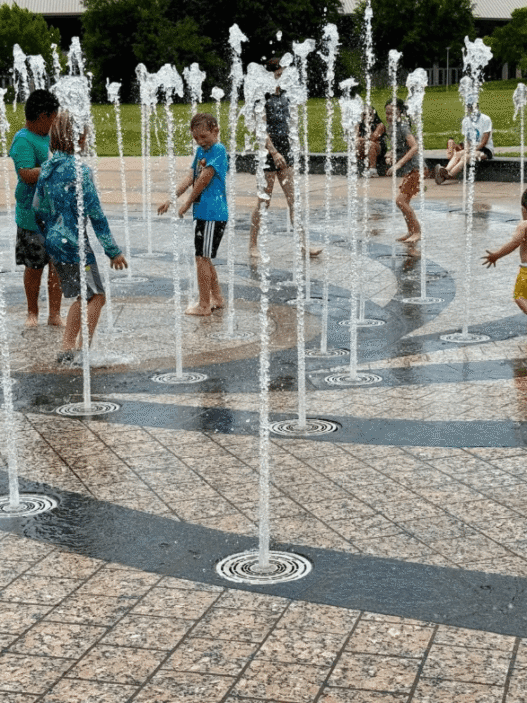 A young child plays in a splash pad at Liz Carpenter Fountain in Austin as families seek relief from extreme heat.