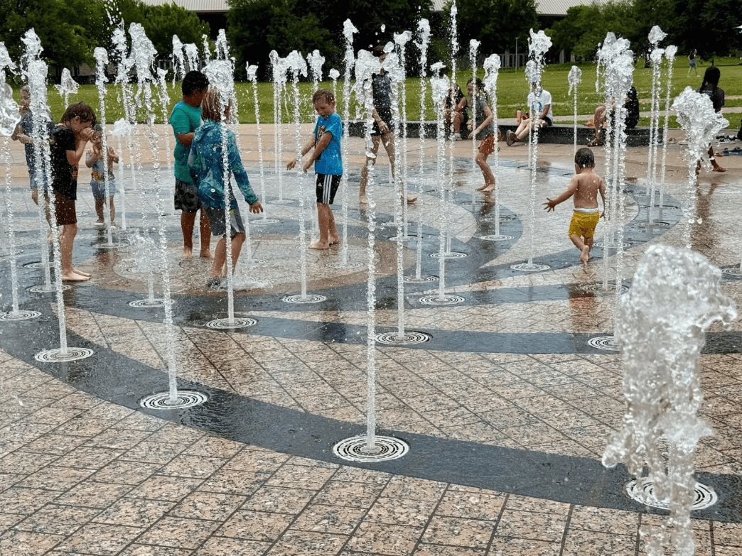 A young child plays in a splash pad at Liz Carpenter Fountain in Austin as families seek relief from extreme heat.
