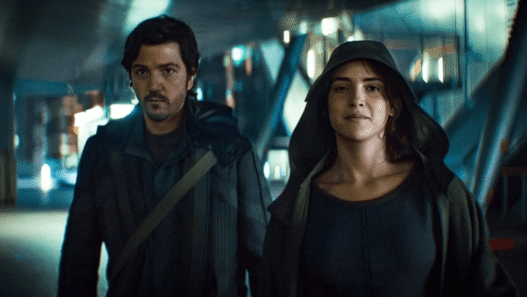 Cassian Andor stands amid a chaotic street scene during the Ghorman uprising in Andor Season 2, Episode
