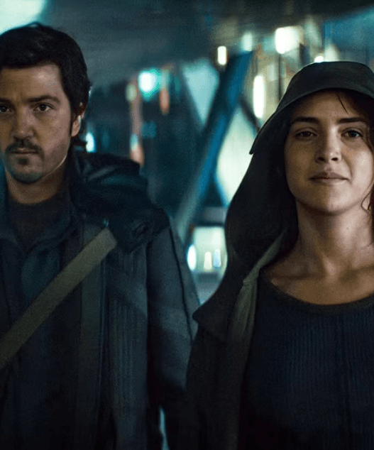 Cassian Andor stands amid a chaotic street scene during the Ghorman uprising in Andor Season 2, Episode