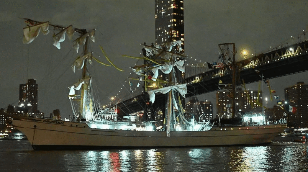 Mexican Navy tall ship Cuauhtémoc with broken masts after striking the Brooklyn Bridge, with crew members visible in the rigging and emergency response underway.