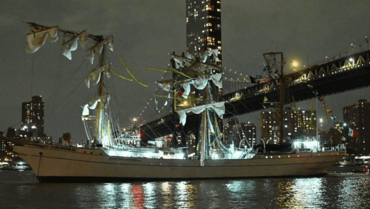 Mexican Navy tall ship Cuauhtémoc with broken masts after striking the Brooklyn Bridge, with crew members visible in the rigging and emergency response underway.