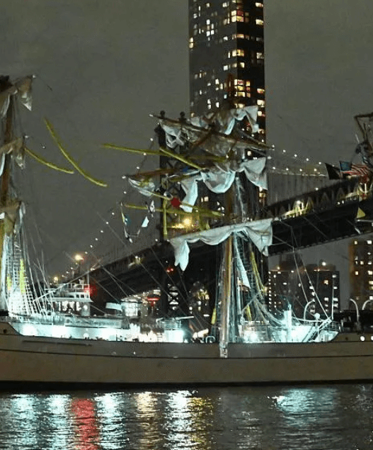 Mexican Navy tall ship Cuauhtémoc with broken masts after striking the Brooklyn Bridge, with crew members visible in the rigging and emergency response underway.